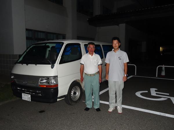 ブルーシート100枚を乗せた車の前で市民安全課山本 寿幸課長と森本 良太主査が映っている写真